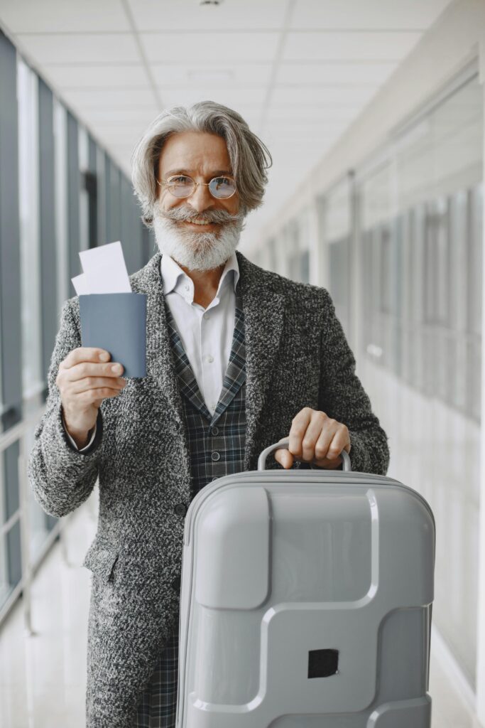 pexels-photo-6050136-6050136 Elderly man in airport holding passport and luggage, smiling confidently at the camera.